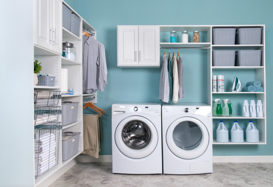 Select laundry room with washer and dryer unit, shelves, laundry baskets and hanging clothes with blue walls.
