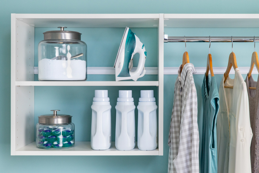 Select laundry room with storage cabinets with hanging clothes with blue wall.