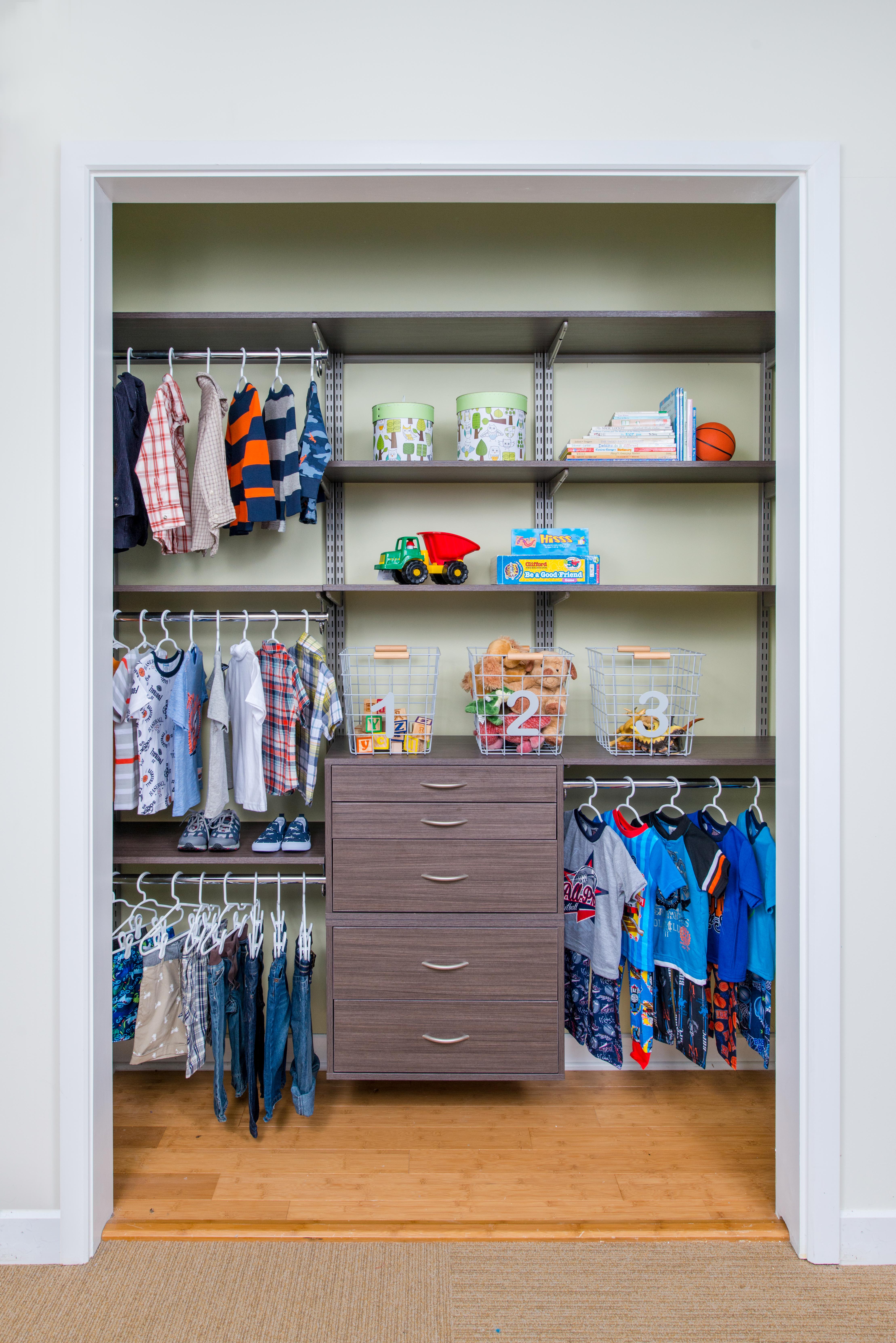 Boys Reach-In Closet in Driftwood Live with green background, 3 tiered shelves on the left and 2 tiered shelves on the right with toys and drawers in the middle.