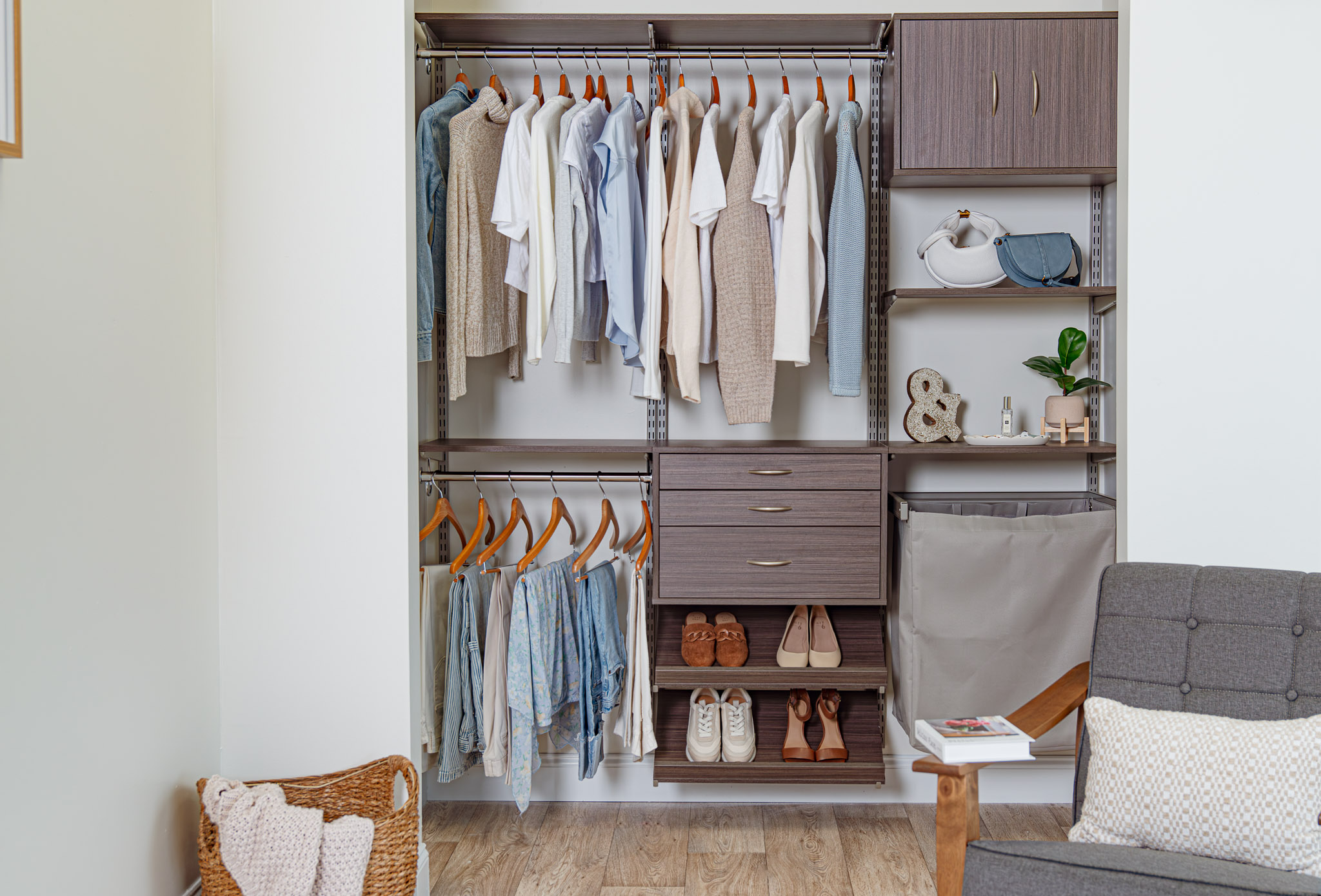 Driftwood Live Reach-in Women's Closet with neutral and blue clothing and accent chair in corner.