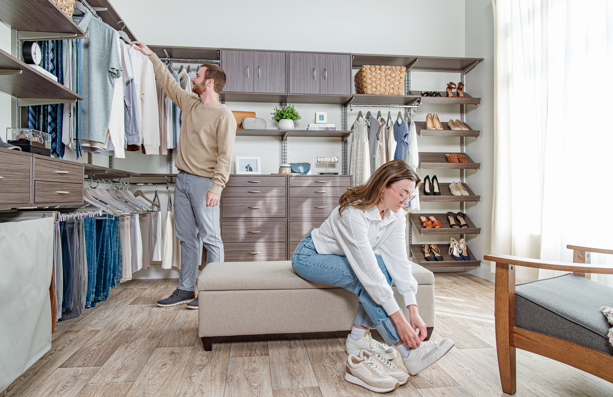 freedomRail Bedroom in Driftwood Live with male model grabbing a shirt and female model sitting on bench with neutral clothing.