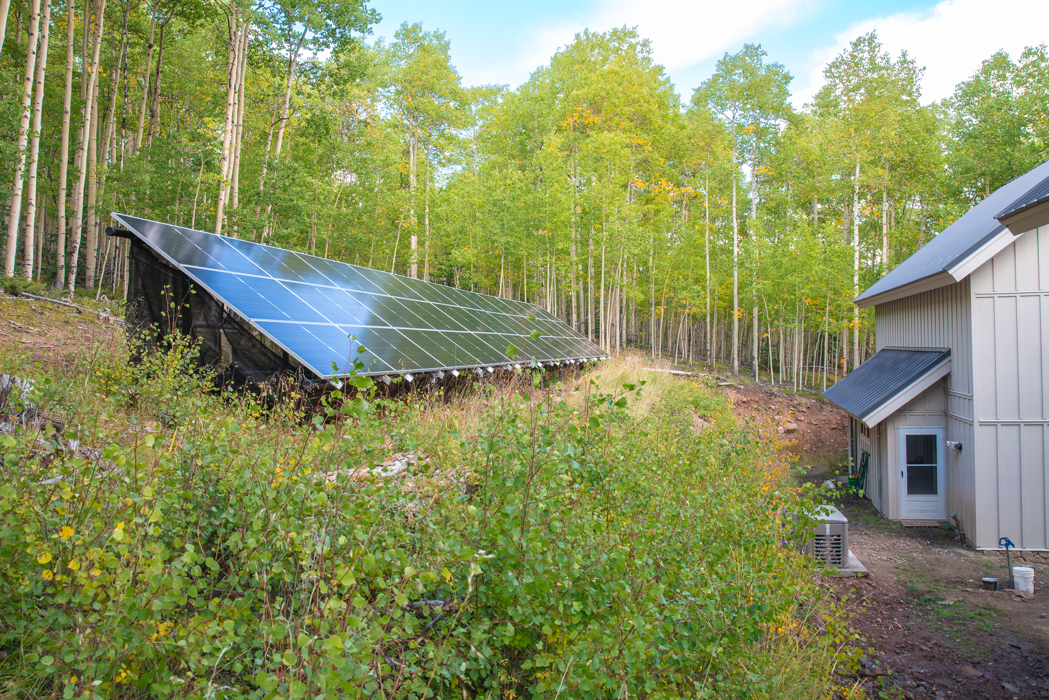 Mariposa Meadows Compound Exterior showcasing solar panels, greenery, and house in the right corner.