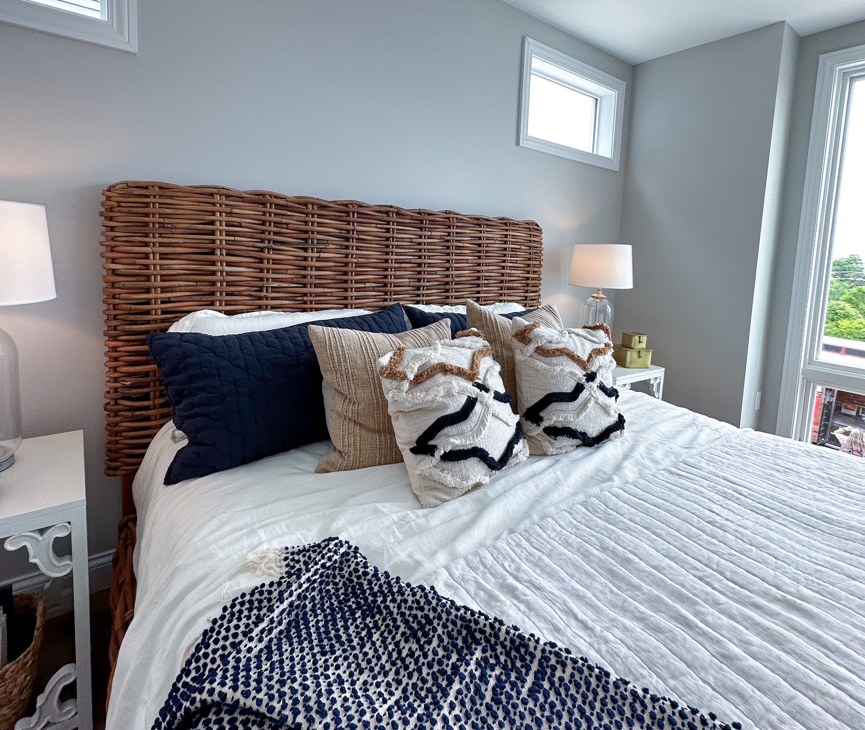 Primary Bedroom at Homearama 2023 with textured bedding, navy accents, and wicker headboard.