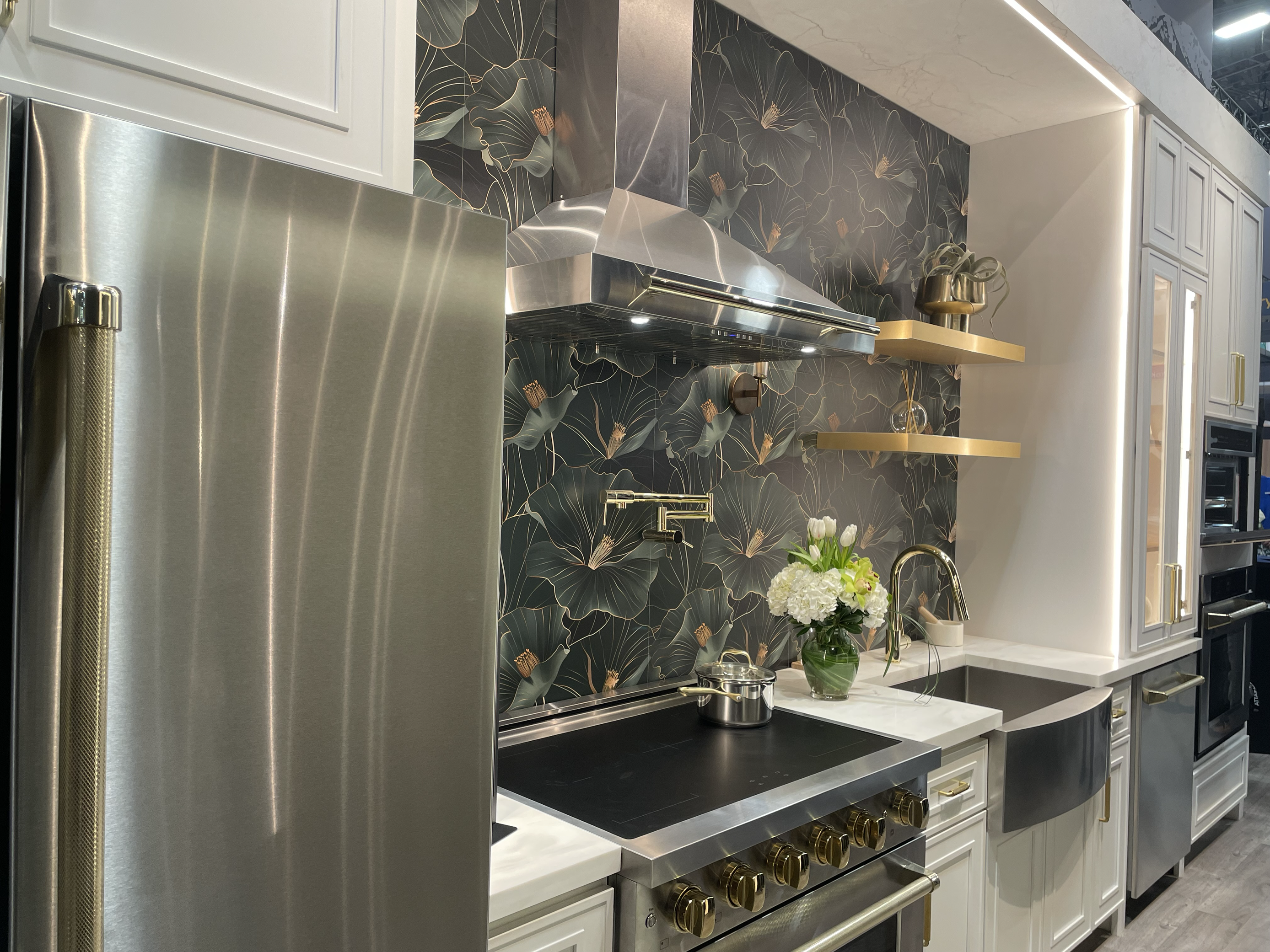 Dark Kitchen Display at IBS 2025 with stainless steel refrigerator, dark and moody floral wallpaper, and gold shelves.