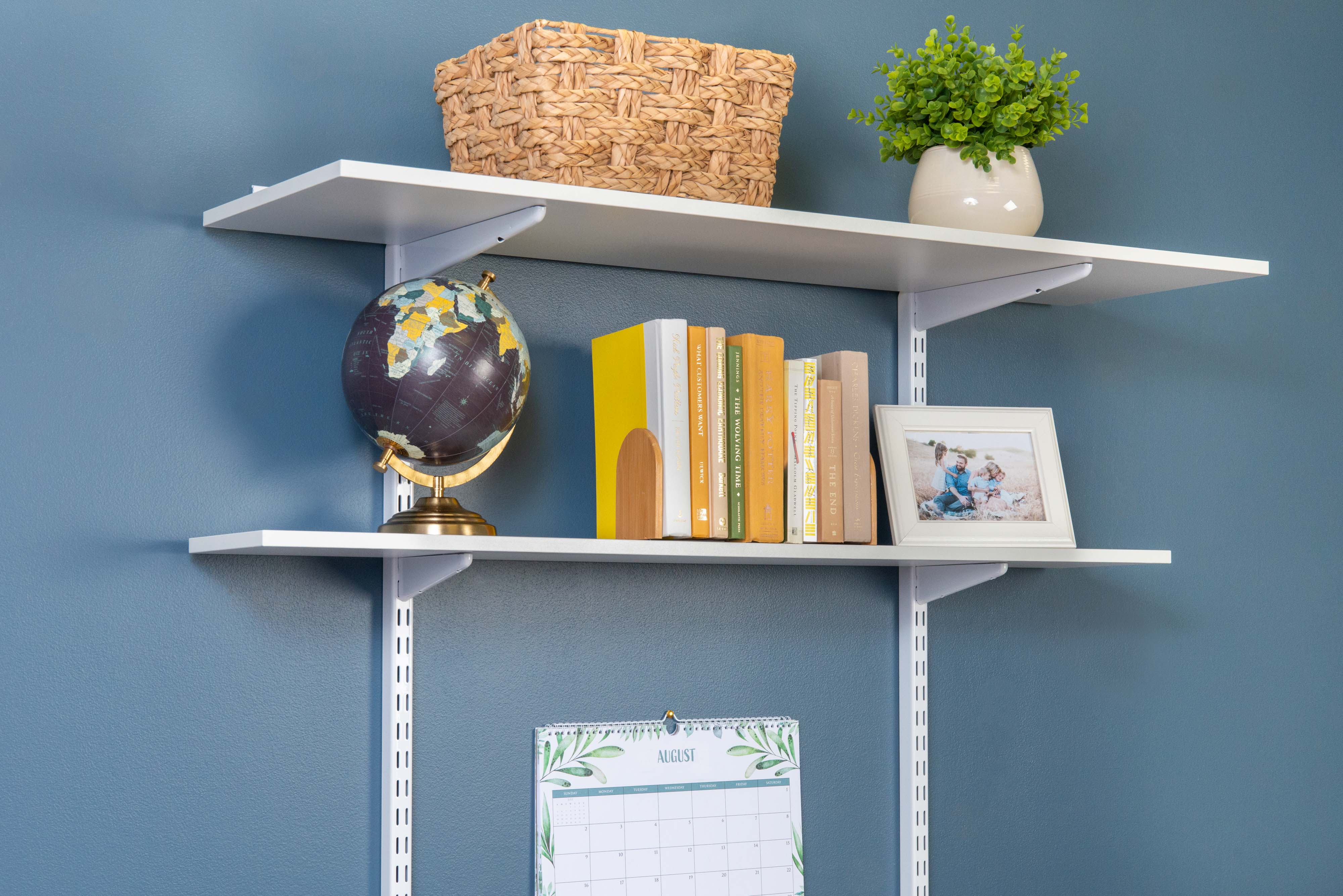 freedomRail White Desk close up with globe, books, picture, plant, calendar, and wicker basket.