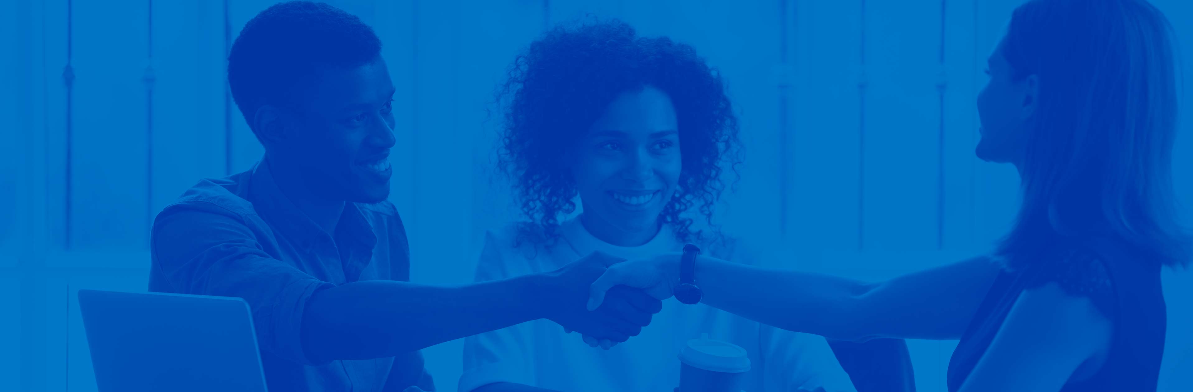 couple shaking hands with a woman over a table. There is a blue overlay over the image.