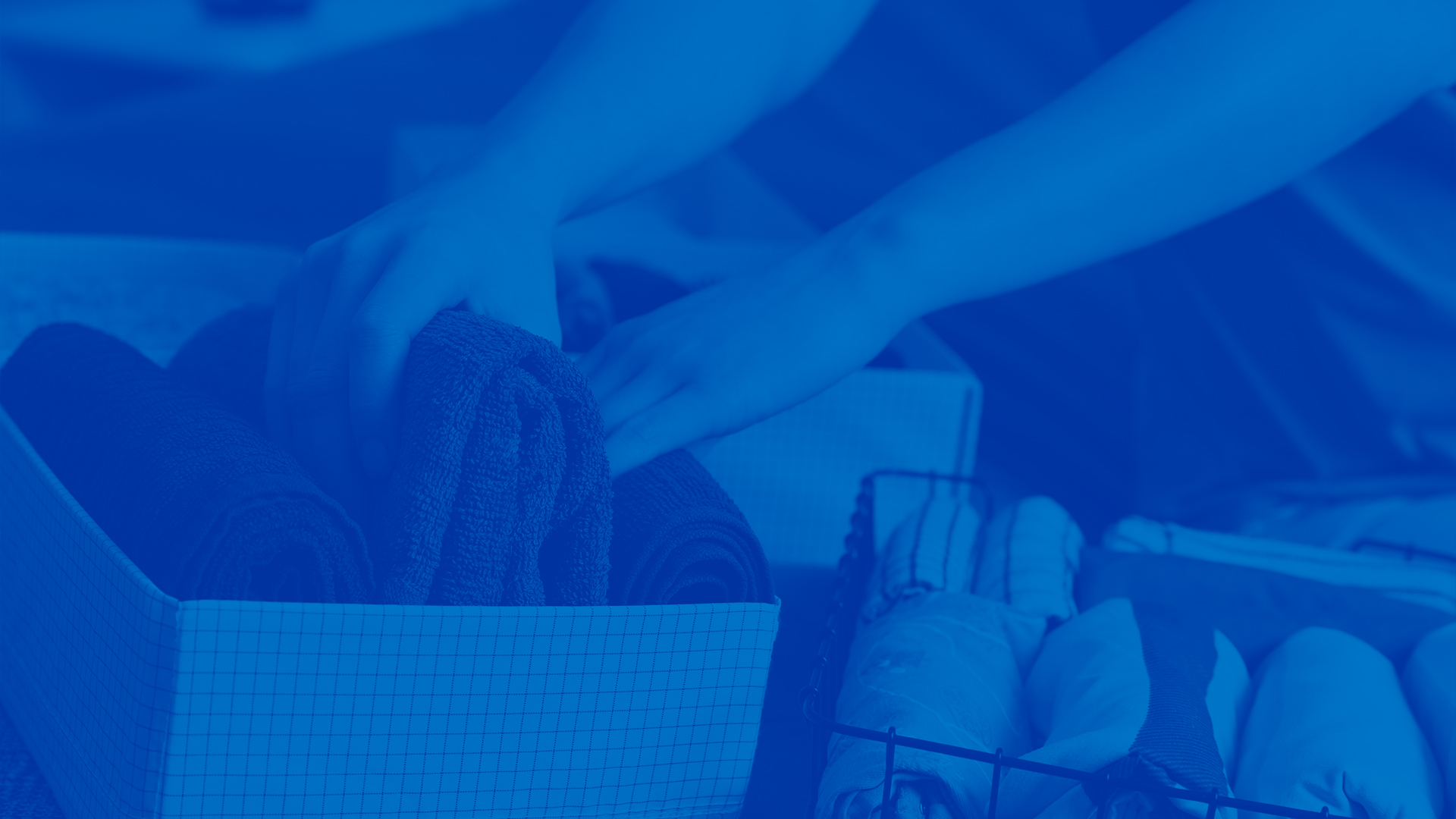 This image is a photo of a woman folding clothes and organizing them into bins. The image has a blue overlay.