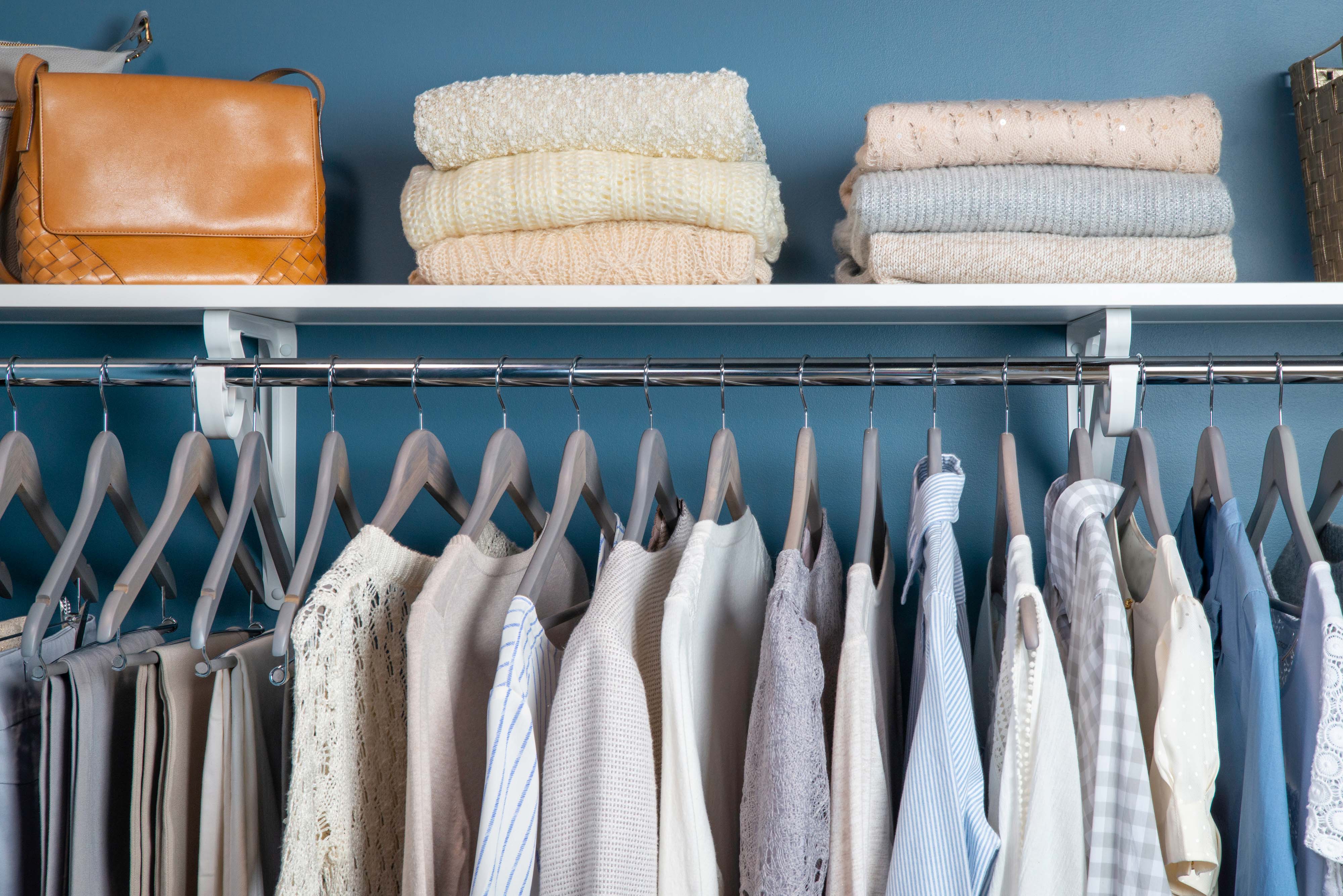 VUE closet in white with clothes hanging and brown woven baskets on the shelf.