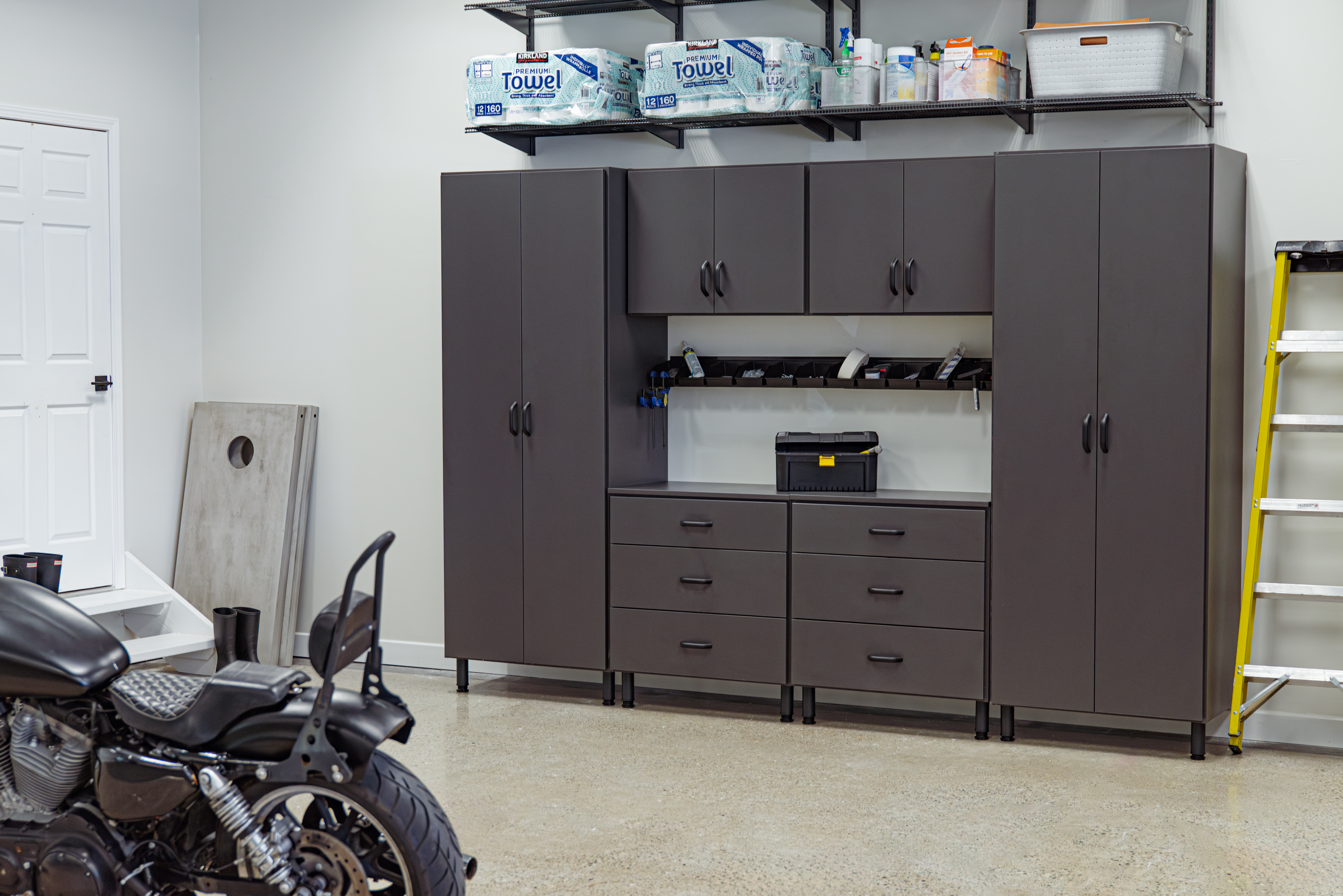 Single Family home garage with garage system on back wall, motorcycle up close blurred out, bright yellow ladder next to system, and entry door in far left corner.