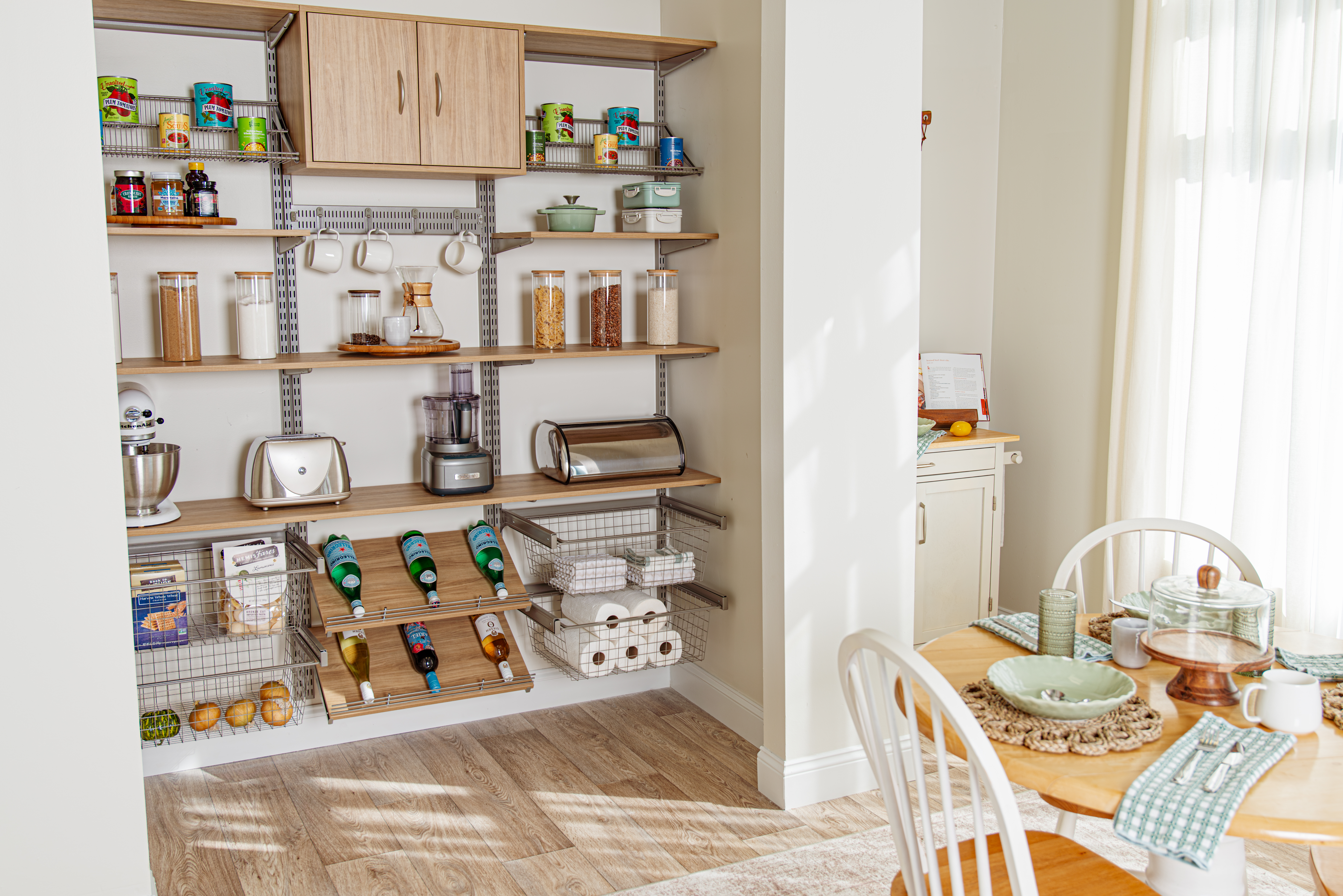 freedomRail Reach-in Pantry in Blonde Oak with dining table in right bottom corner, dry goods organized in pantry and soft natural lighting.