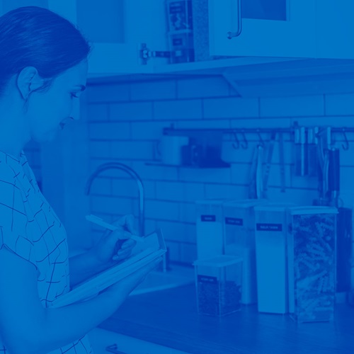 Professional Organizer making notes within a kitchen on the items placed in front of her, all with a blue overlay on the entire image.