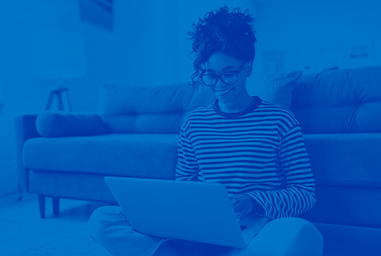 woman on laptop shopping in front of her couch sitting on the floor wearing a stripped shirt. There is a blue overlay over the entire image